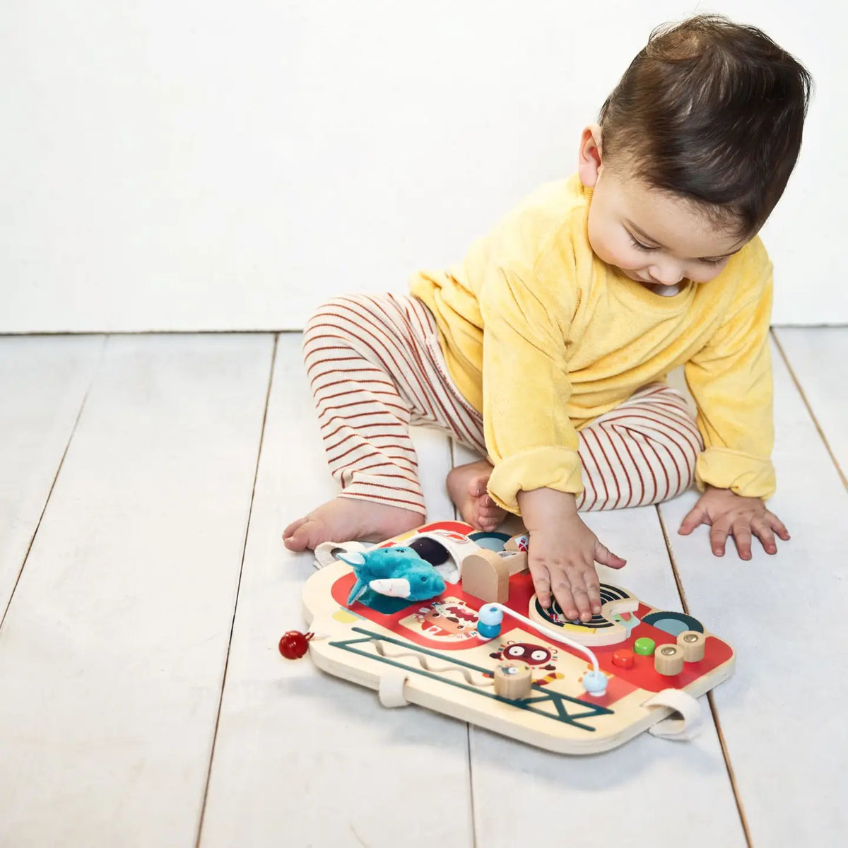 Child playing with a colorful wooden toy on a light wooden floor.