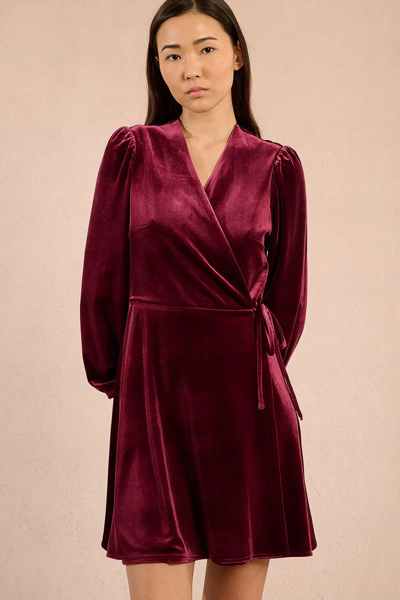 Woman wearing a dark red velvet dress against a beige background