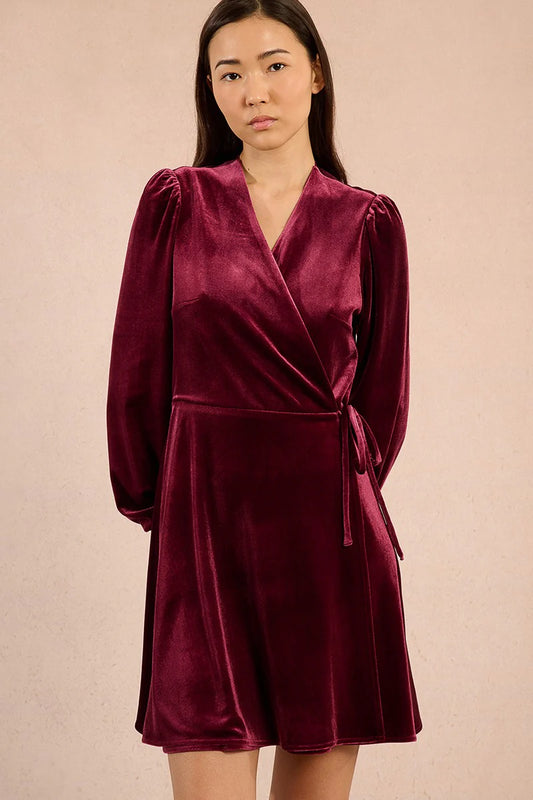 Woman wearing a dark red velvet dress against a beige background