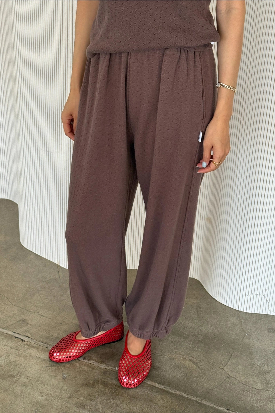 Person wearing brown pants and red shoes standing against a white curtain.