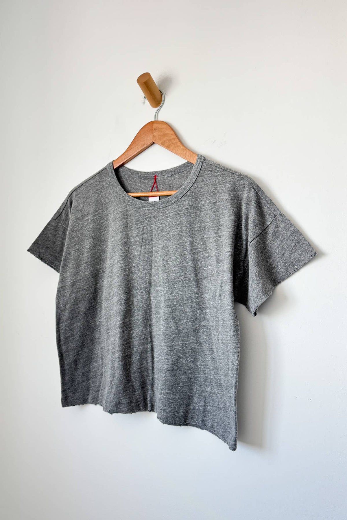 Gray t-shirt on a wooden hanger against a white background