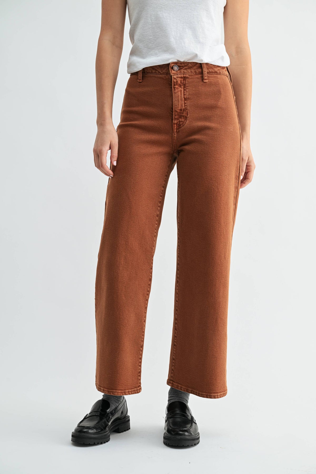 Person wearing brown jeans and black shoes on a white background
